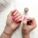 Close-up of a woman applying glitter nail polish to manicured pink fingernails.