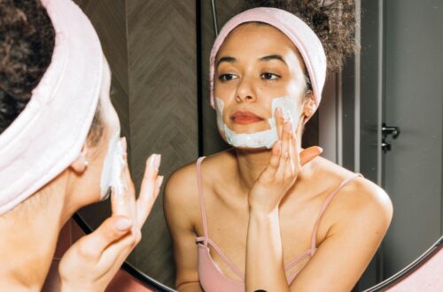 Young woman applying a face mask while looking in the mirror, enjoying her skincare routine.