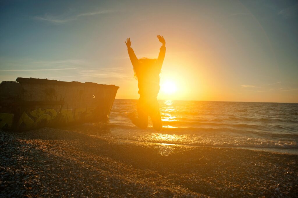 Silhouette of a woman jumping joyfully on a beach at sunset, capturing freedom and happiness.